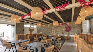 A restaurant with wicker chairs and tables, stone walls, and hanging wicker lamps. - Alexandros Mykonos (Mykonos)
