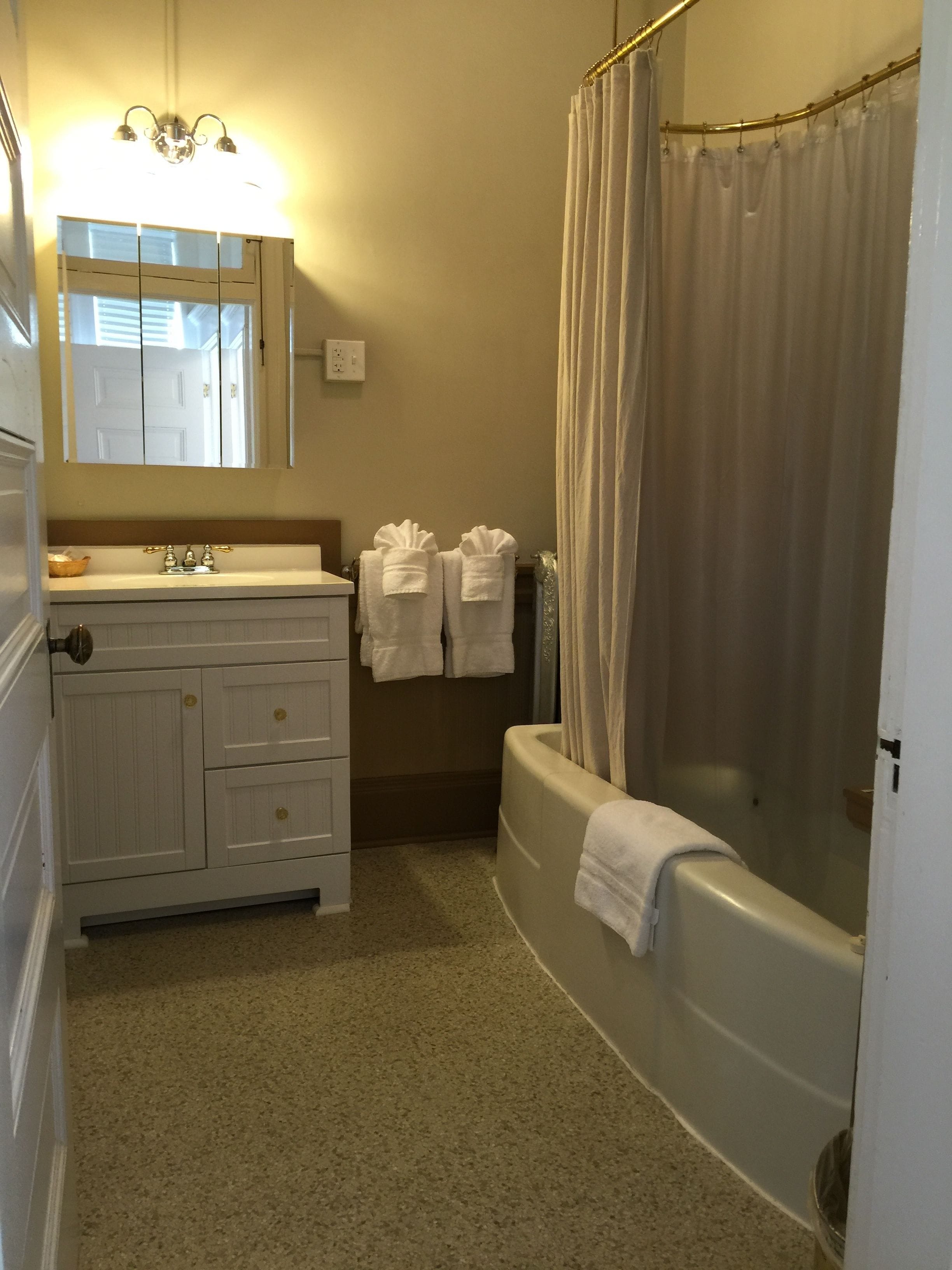 A bathroom with a bathtub, a shower curtain, a sink with a mirror, and two towels hanging on the wall.