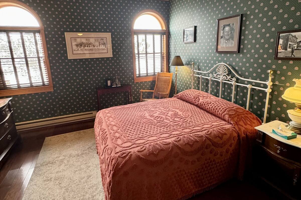A bedroom with a large bed, two windows, a dresser, and a chair.