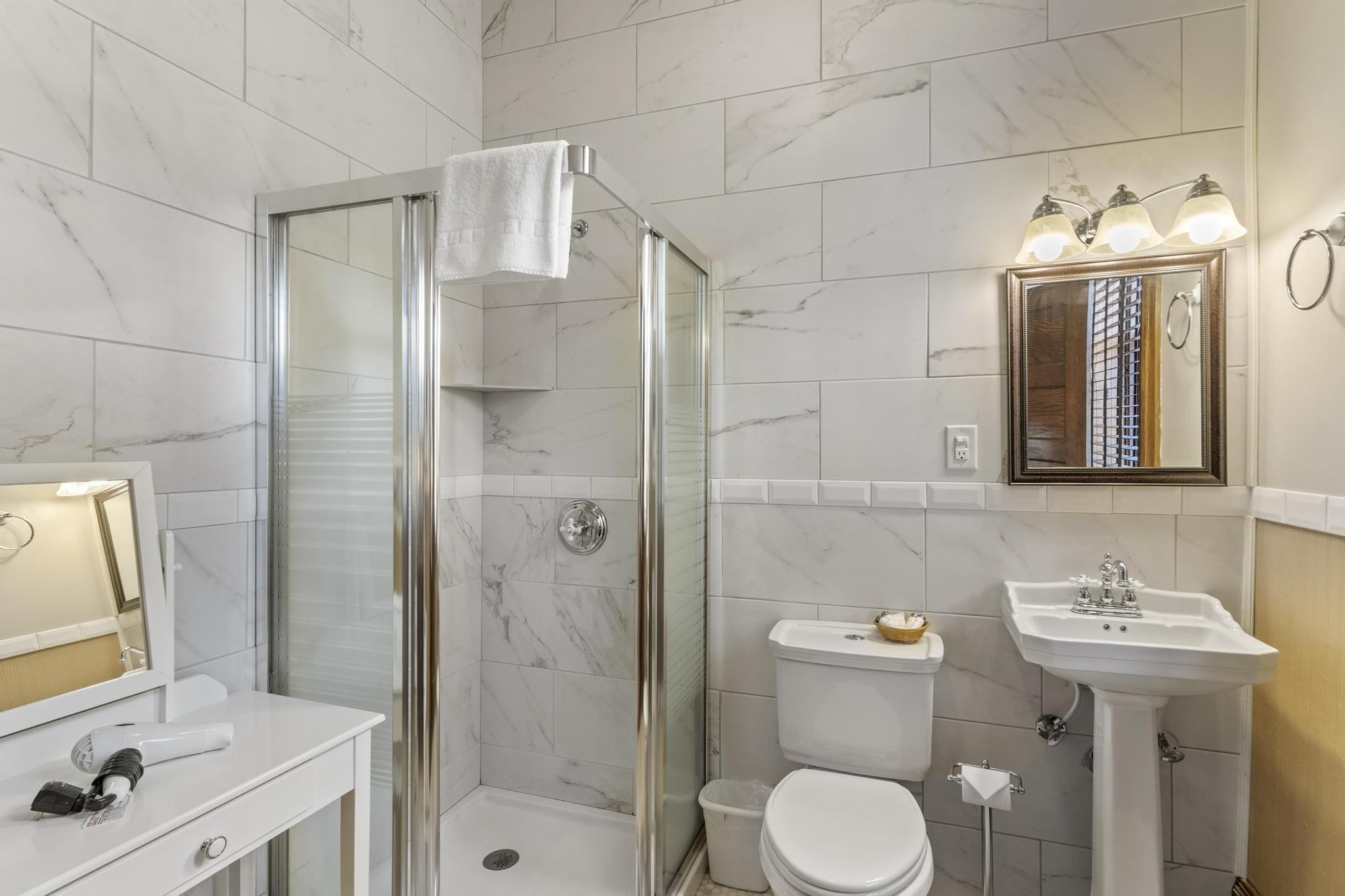 A bathroom with a glass-enclosed shower, a white sink, and a mirror with lights.