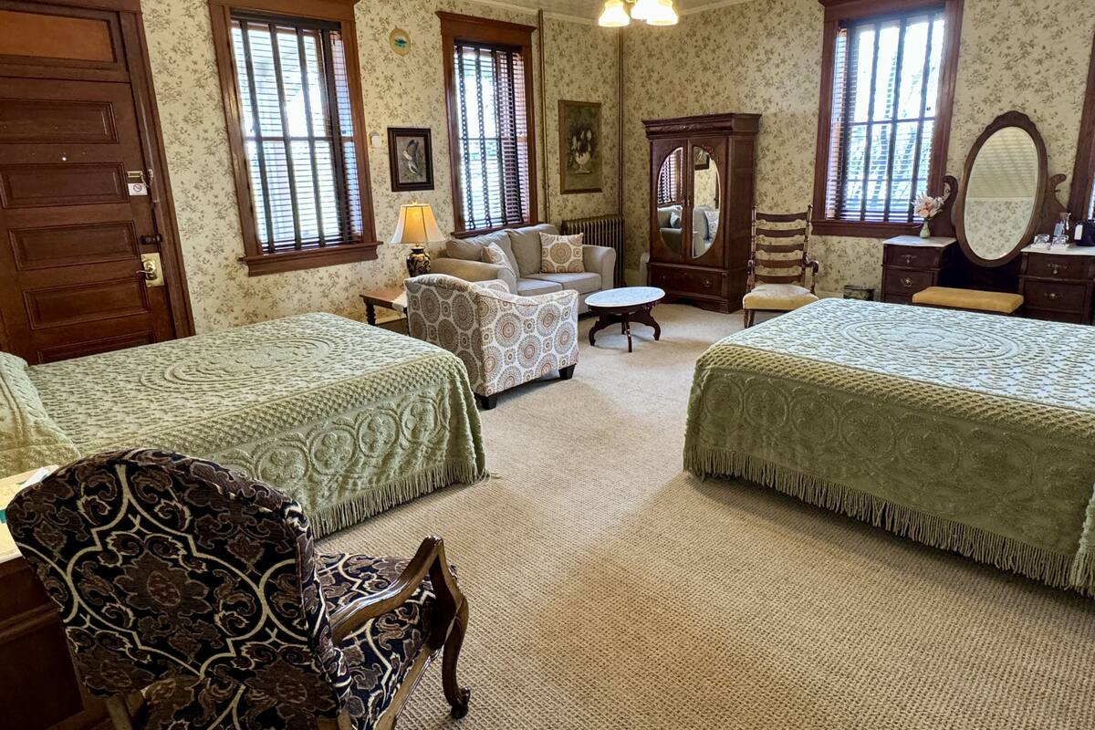 A room with two beds, a sofa, a chair, a table, and a dresser.