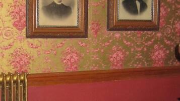 Two framed portraits on a wall with floral wallpaper, a radiator, and a chest of drawers.