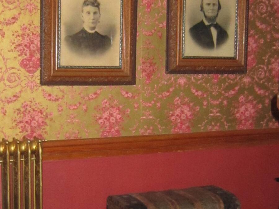 Two framed portraits on a wall with floral wallpaper, a radiator, and a chest of drawers.