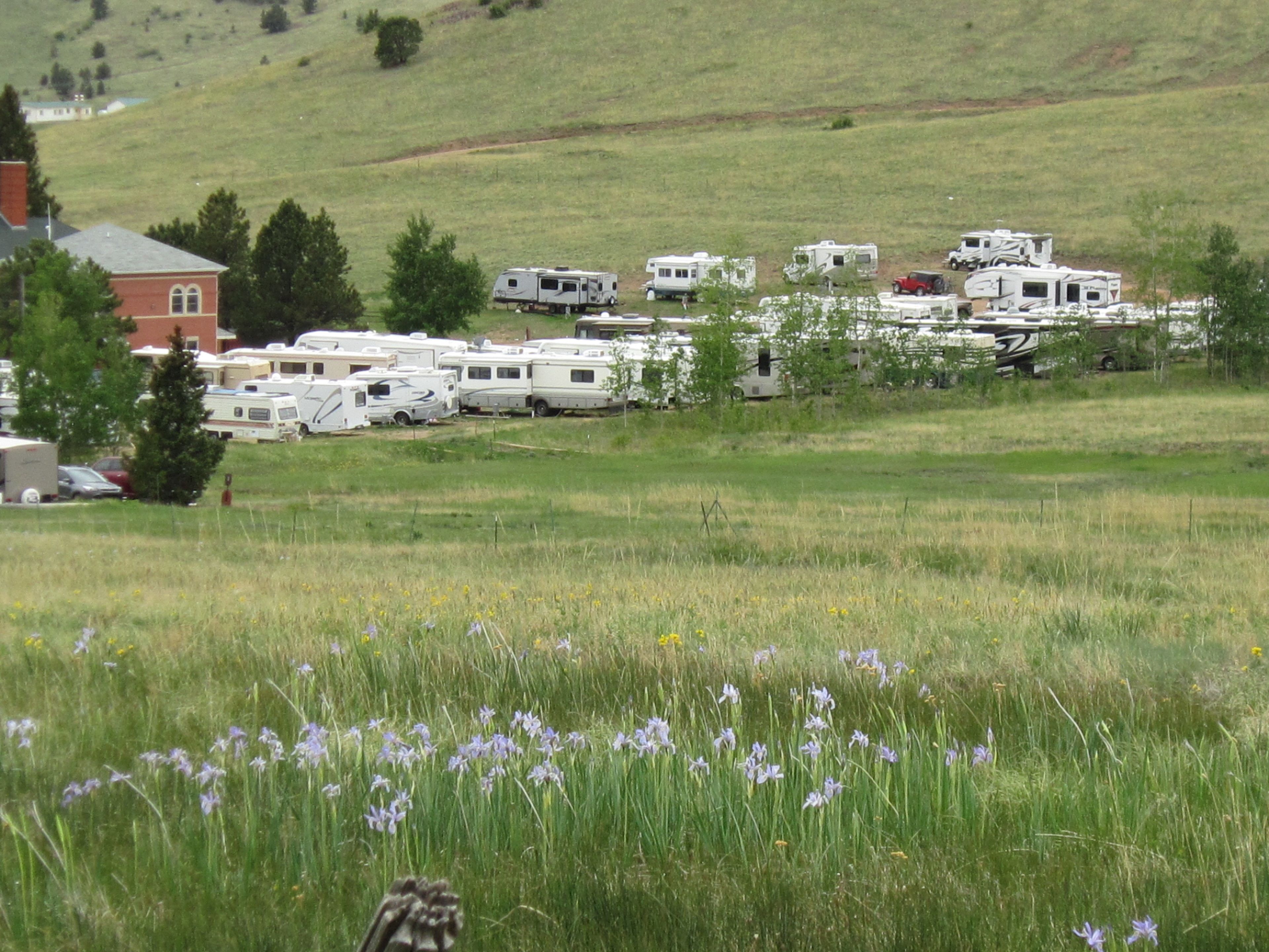 Un champ où sont stationnés de nombreux camping-cars sur une colline herbeuse, avec un bâtiment en arrière-plan.