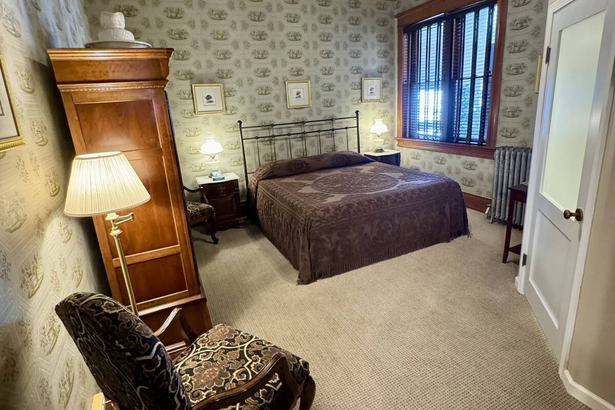 A bedroom with a bed, a chair, a dresser, a ceiling fan, and a window with blinds.