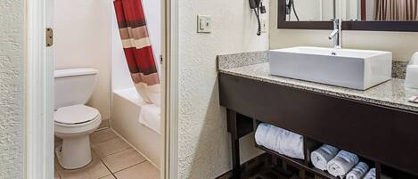 A bathroom with a white sink, a towel rack with towels, a toilet, and a shower curtain.