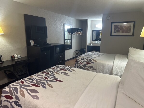Une chambre d’hôtel avec deux lits, un bureau avec un ordinateur, une télévision et un miroir.