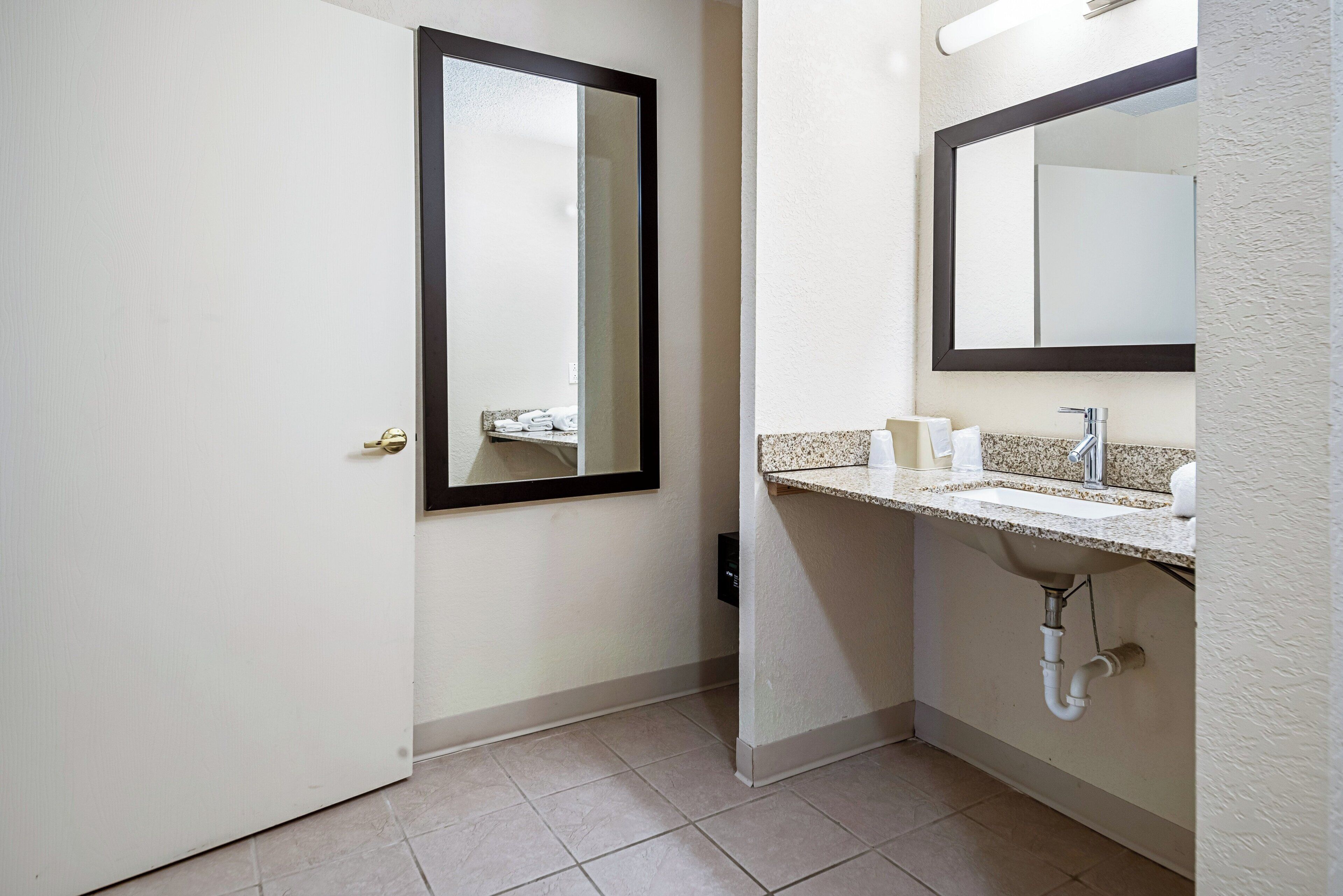 A bathroom with a door, a mirror, a sink, and a towel rack.