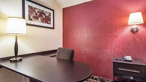 Una habitación de hotel con una mesa de conferencias, una silla, un escritorio con teléfono y una lámpara de pared.