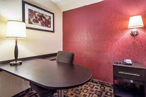 A hotel room with a conference table, a chair, a desk with a telephone, and a wall-mounted lamp. - Red Roof Inn Anderson, IN (Anderson)
