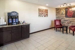 A hotel lobby with a coffee station, a seating area with a red leather chair, and a wall with a Red Roof Inn sign. - Red Roof Inn Anderson, IN (Anderson)