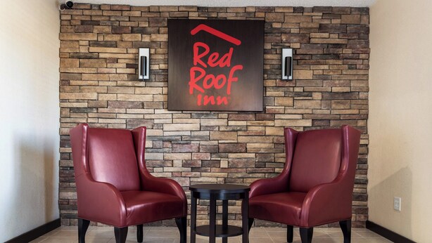 Un vestíbulo de Red Roof Inn con pared de piedra, dos sillones de cuero y una pequeña mesa.