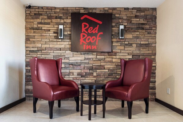 A Red Roof Inn lobby with a stone wall, two leather chairs, and a small table. - Red Roof Inn Anderson, IN (Anderson)