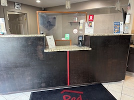 Un mostrador de recepción de hotel con un reloj digital, una foto enmarcada y un letrero de Red Roof.