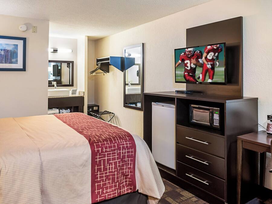 Quarto de hotel com cama, televisão, micro-ondas, cafeteira e escrivaninha com gavetas.