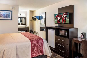 Habitación de hotel con cama, televisión, microondas, cafetera y escritorio con cajones.