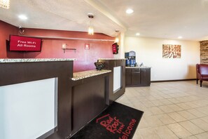 A hotel reception area with a digital screen displaying 'Free Wi-Fi All Rooms' and a 'Red Roof Inn Welcome' mat. - Red Roof Inn Anderson, IN (Anderson)
