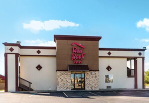 A Red Roof Inn building with a stone facade, a flat roof, and a parking lot in front. - Red Roof Inn Anderson, IN (Anderson)