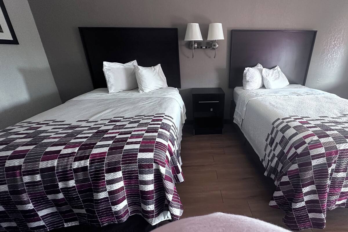 Habitación doble con dos camas, cada una con cubrecama a cuadros, mesita de noche y lámparas de pared.