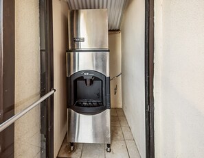 A stainless steel ice dispenser in a narrow hallway with tiled flooring. - Red Roof Inn Anderson, IN (Anderson)