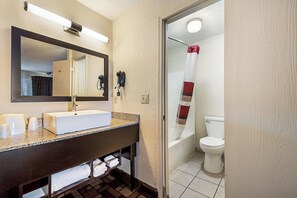 A bathroom with a white sink, mirror, and towel rack. There is a shower curtain with a striped pattern. - Red Roof Inn Anderson, IN (Anderson)