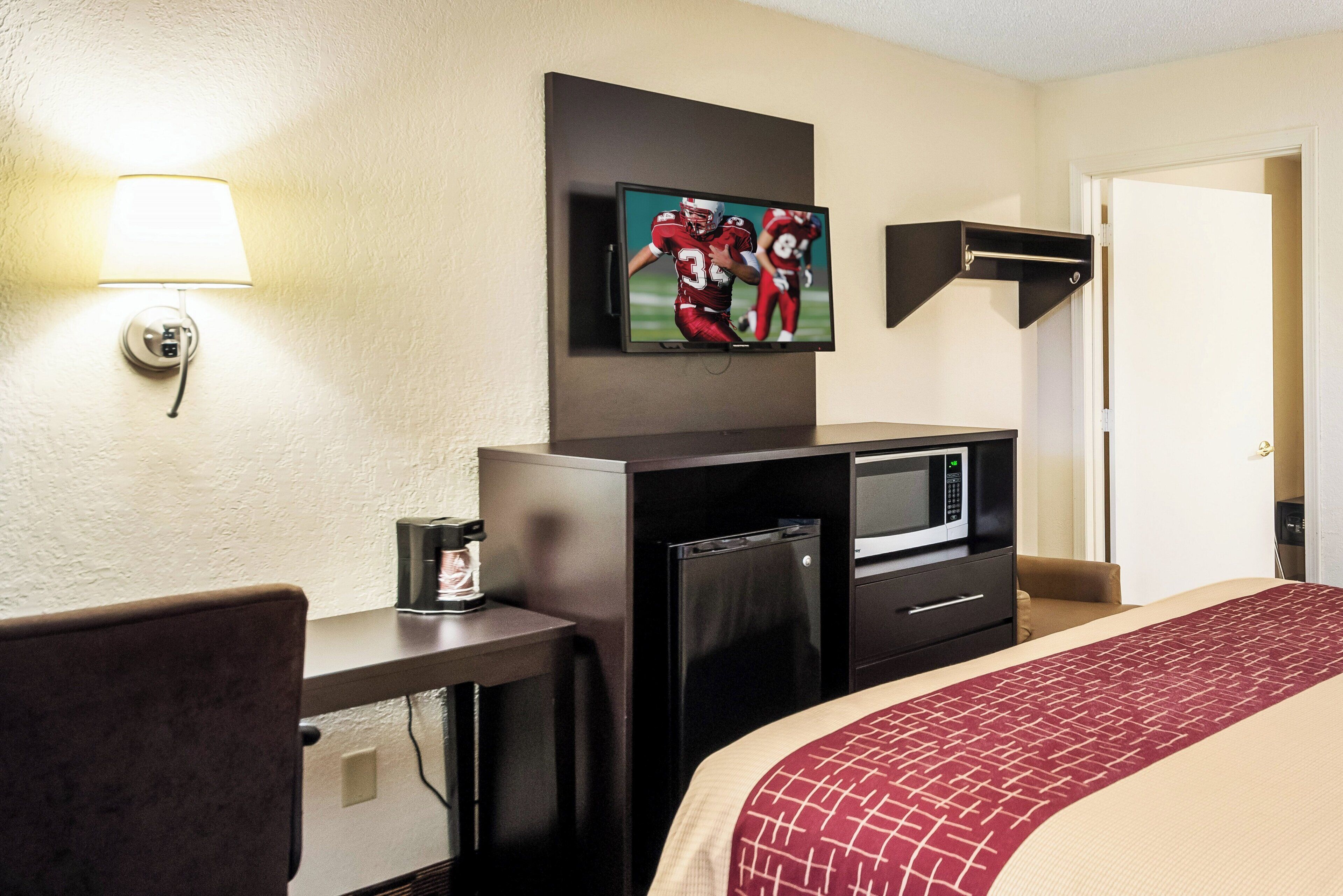 Ein Hotelzimmer mit Bett, Schreibtisch, Wandfernseher, Mikrowelle und einer Kaffeemaschine.