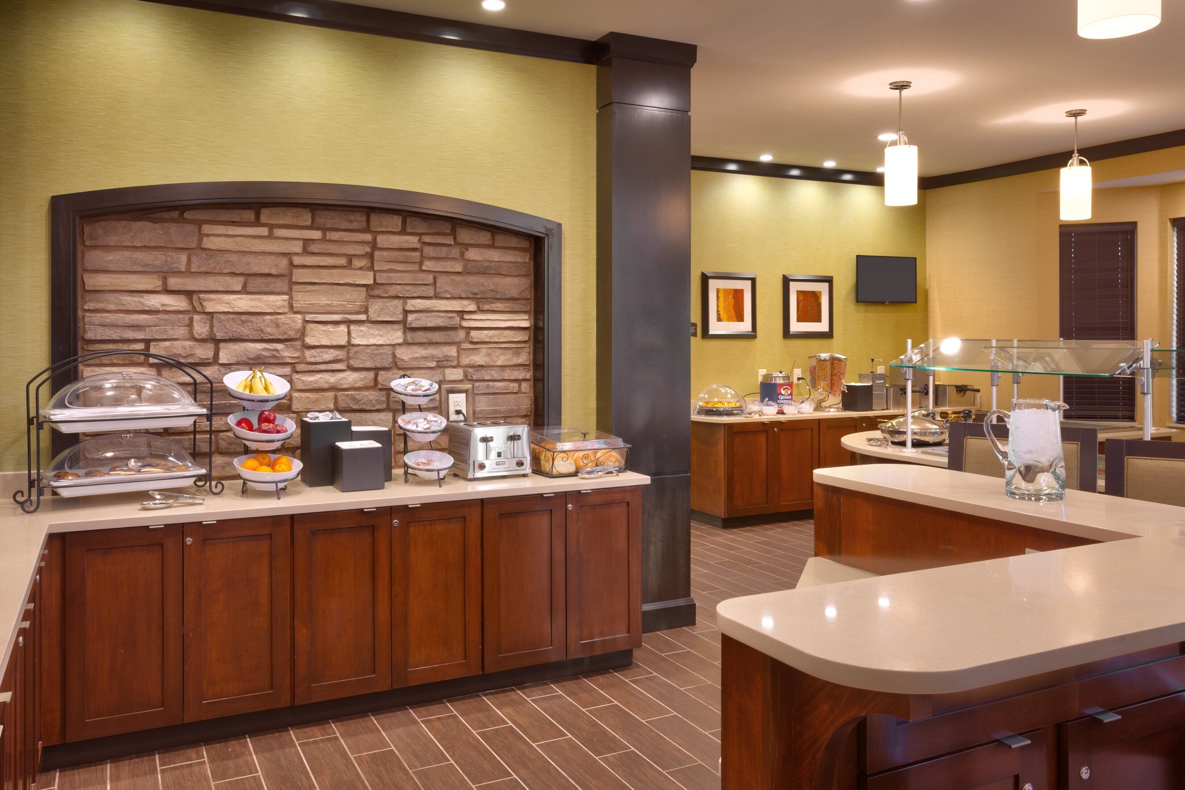 A hotel breakfast area with a stone wall backdrop, buffet setup, and a television screen.