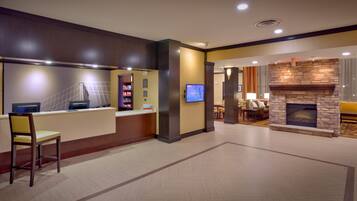 A hotel lobby with a reception desk, a television, a fireplace, and a seating area.