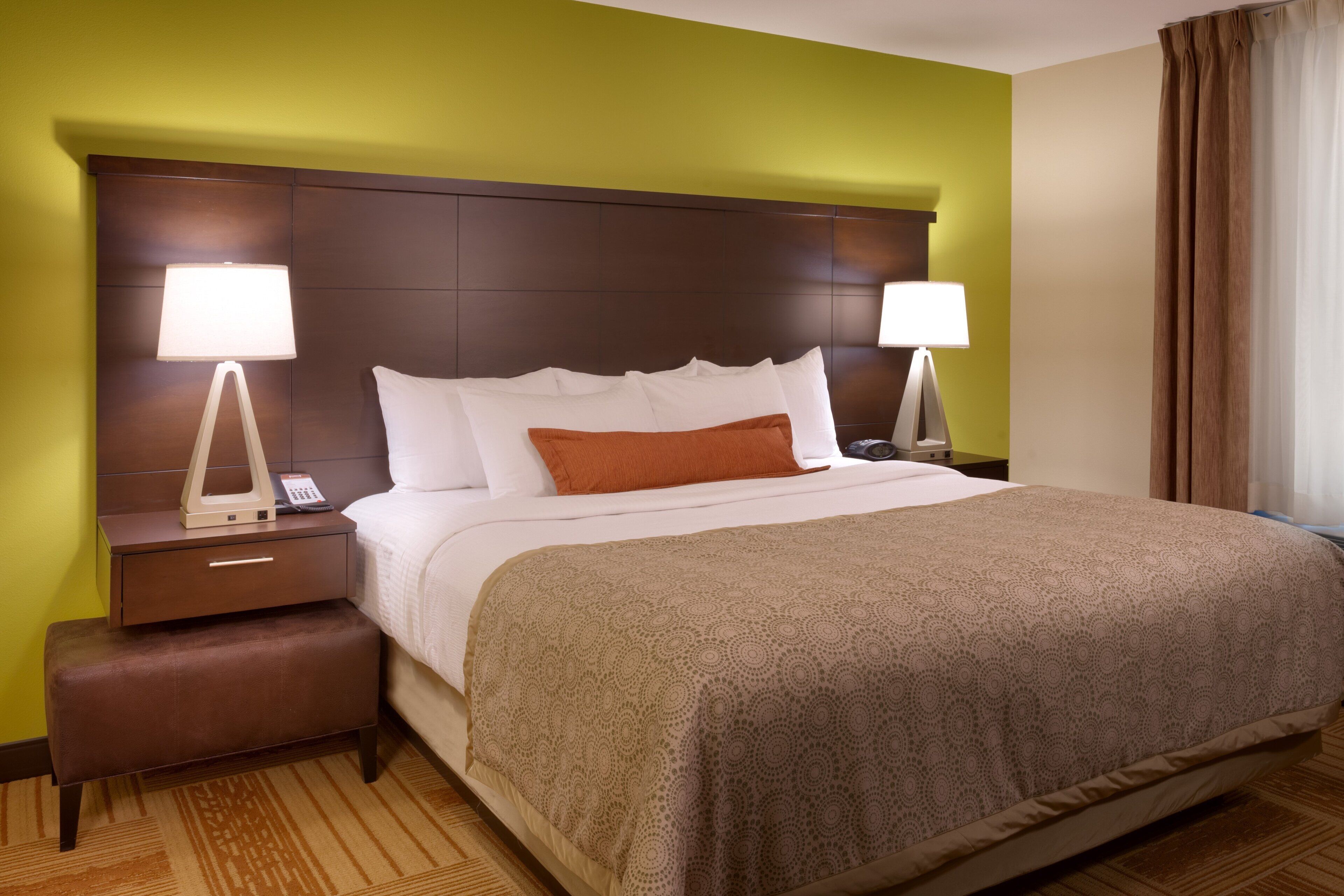 Ein Hotelzimmer mit einem großen Bett, zwei Nachttischen, einer Bank und einem Kopfteil.