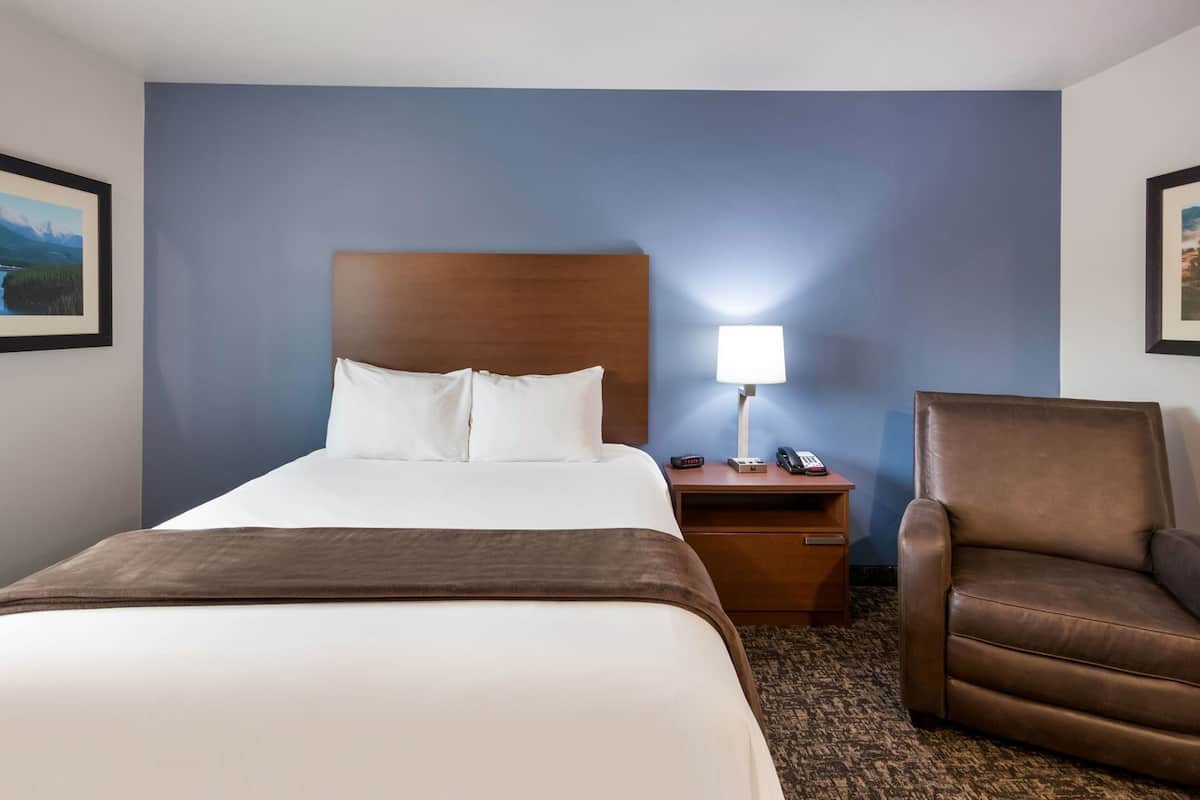 A hotel room with a bed, a nightstand with a lamp, a phone, and a chair.