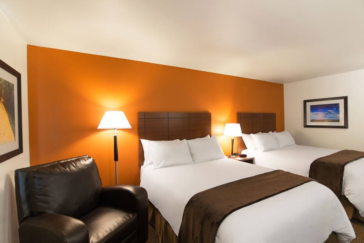 A hotel room with two beds, a chair, a nightstand, and a lamp.