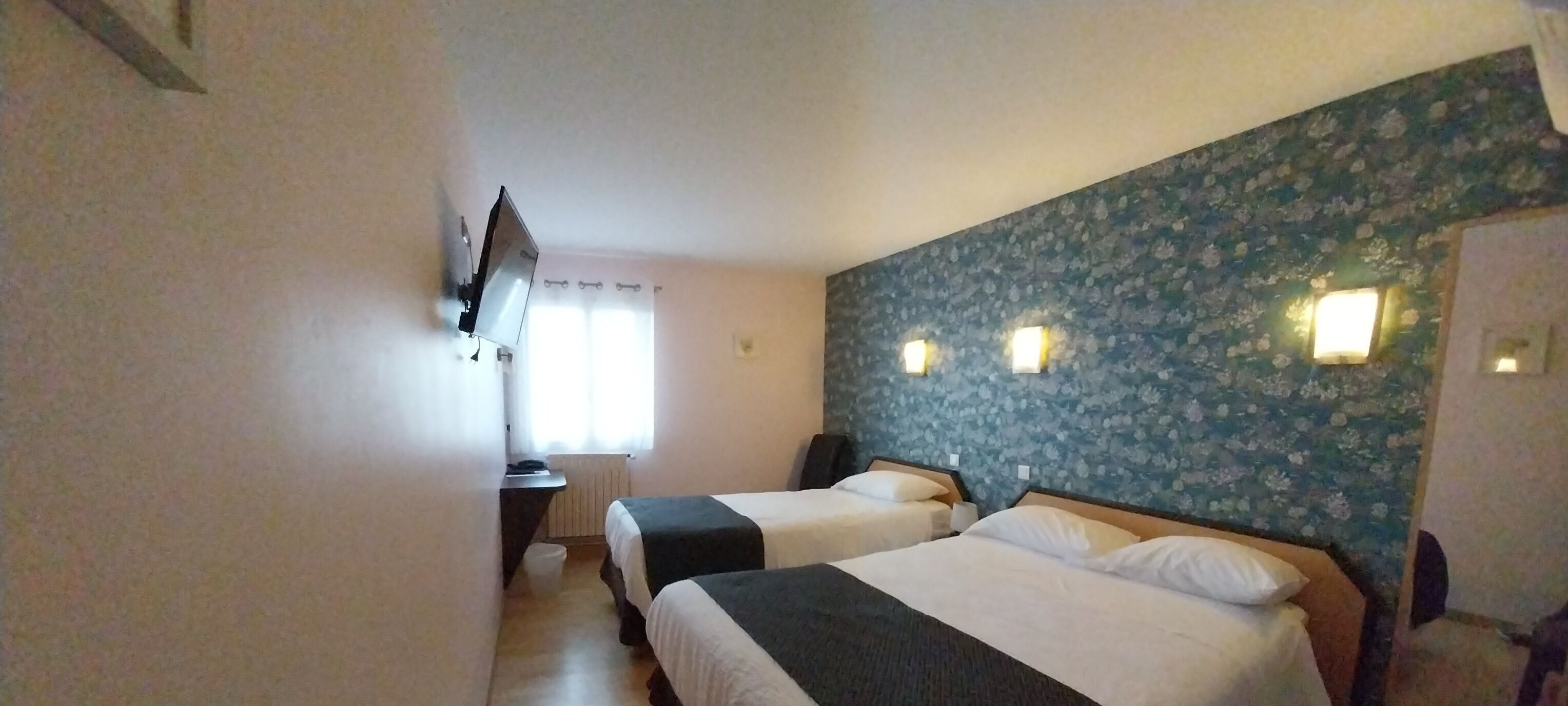 Habitación de hotel con dos camas, un escritorio, una silla, un televisor montado en la pared y una ventana con cortinas.