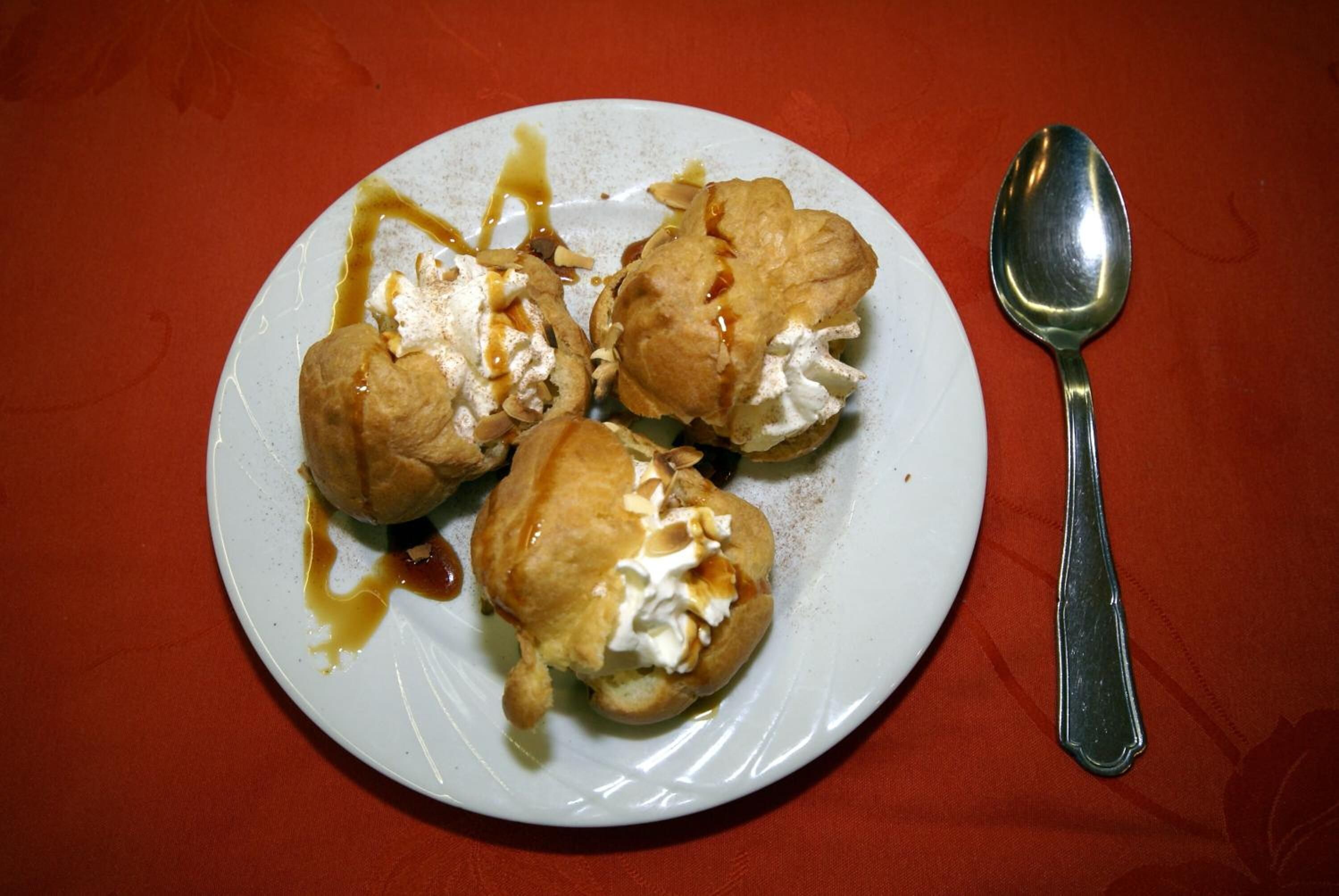 A plate with three pastries and a spoon on a red tablecloth.