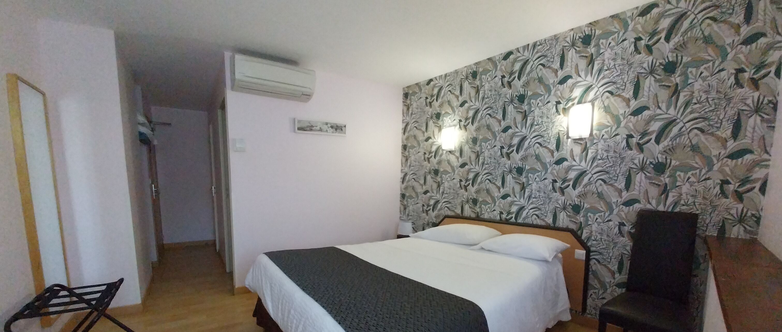 Un dormitorio con cama, una silla, un equipo de aire acondicionado y una pared con estampado floral.