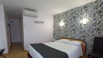 A bedroom with a bed, a chair, an air conditioning unit, and a wall with a floral pattern.