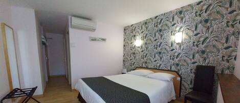 Un dormitorio con cama, una silla, un equipo de aire acondicionado y una pared con estampado floral.