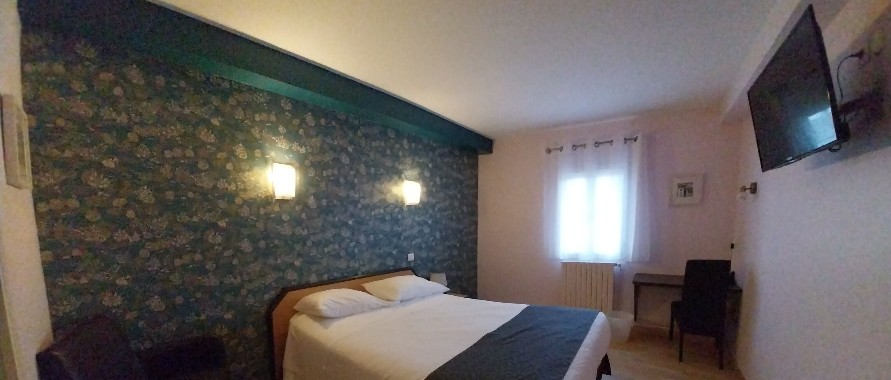 A hotel room with a bed, a desk, a chair, a TV, and a window with curtains.