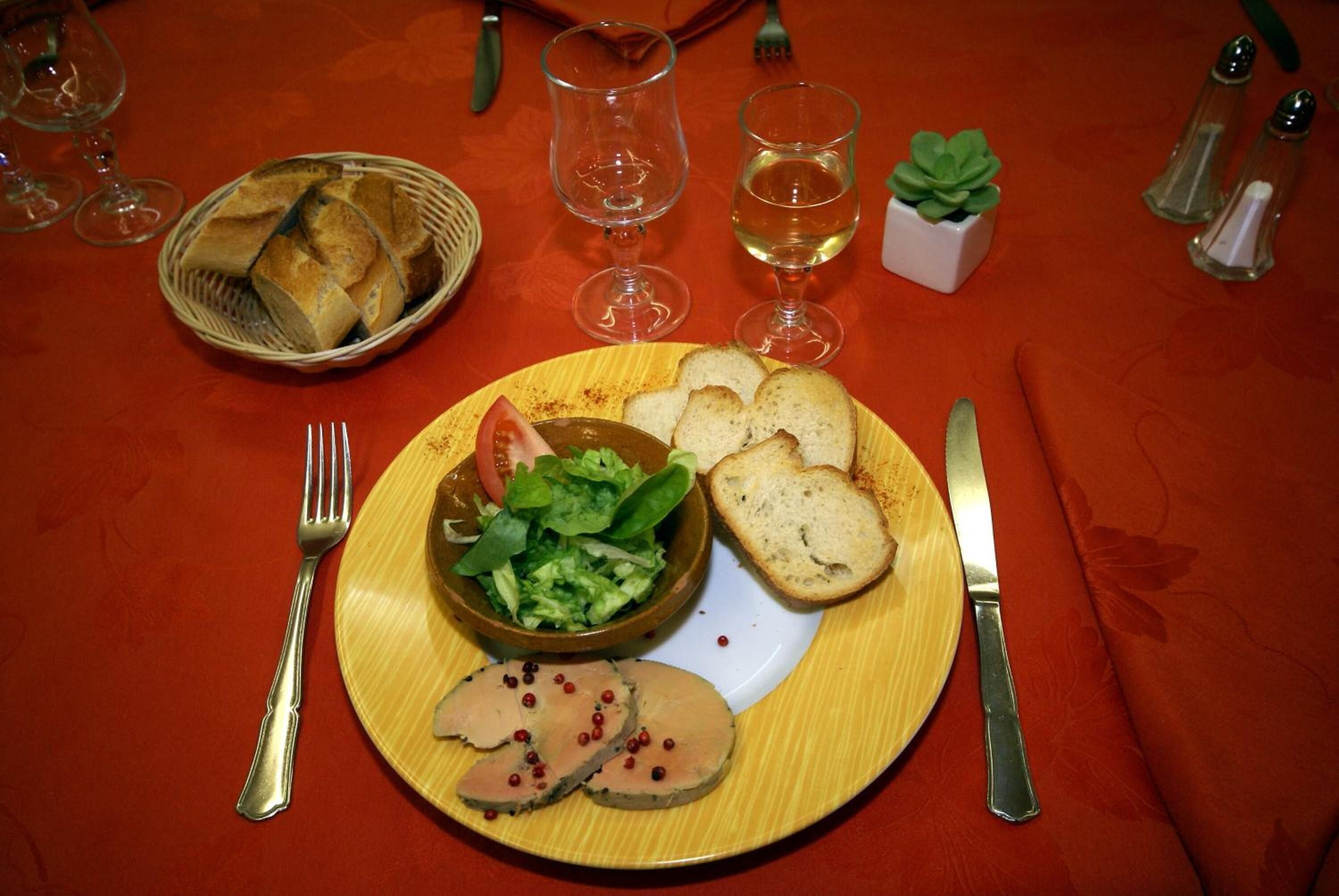 Een eettafel met een bord eten, inclusief brood, salade en vlees, samen met wijnglazen en een kleine plant.