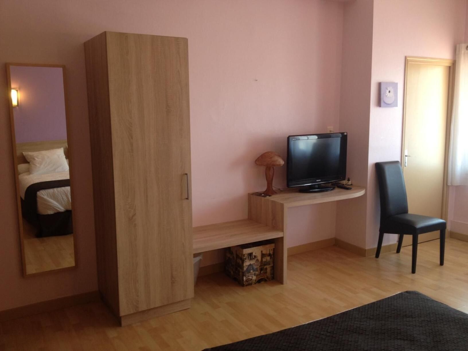 Una habitación con un armario de madera, un televisor sobre un mueble de madera, una silla negra y una cama con ropa de cama blanca.