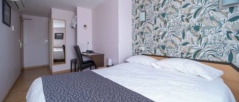 Una habitación de hotel con cama, escritorio, silla y espejo.