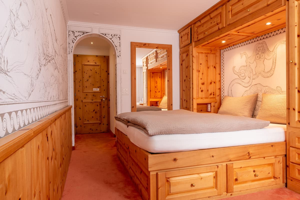 A wooden bedroom with a bed, built-in wardrobe, and a mural on the wall.