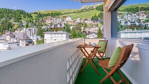 A balcony with a view of a hillside town, wooden chairs, and a small table. - Hotel Arte (St. Moritz)