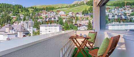 Un balcon donnant sur une ville perchée sur une colline, avec des chaises en bois et une petite table.