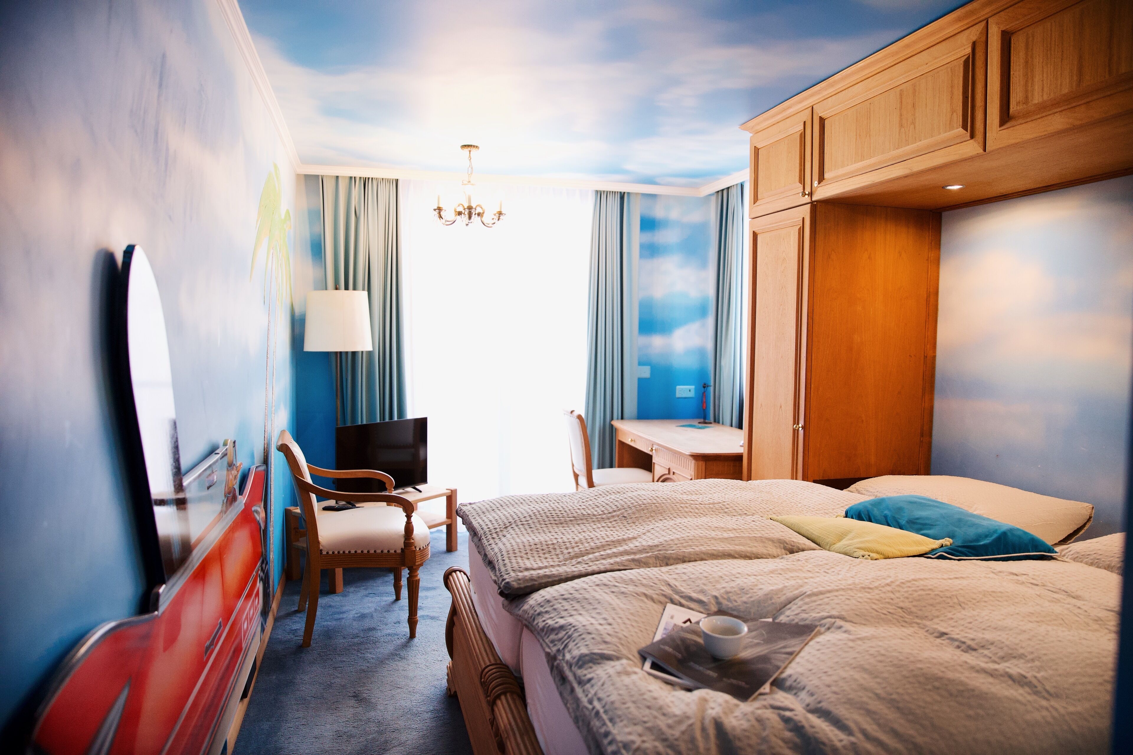 A hotel room with a bed, a desk, a chair, a TV, and a window with curtains.