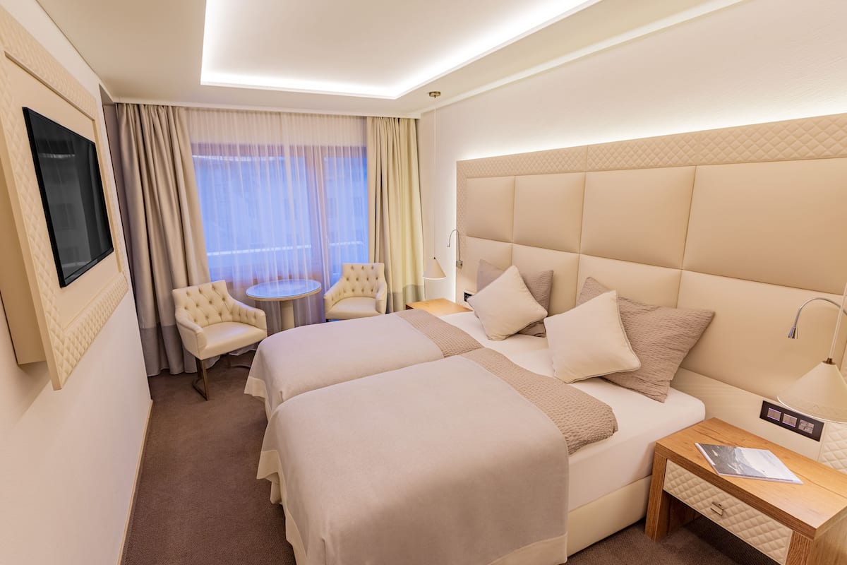 A hotel room with two beds, a TV mounted on the wall, a round table, and a chair.