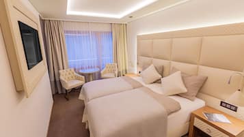 A hotel room with two beds, a TV mounted on the wall, a round table, and a chair.