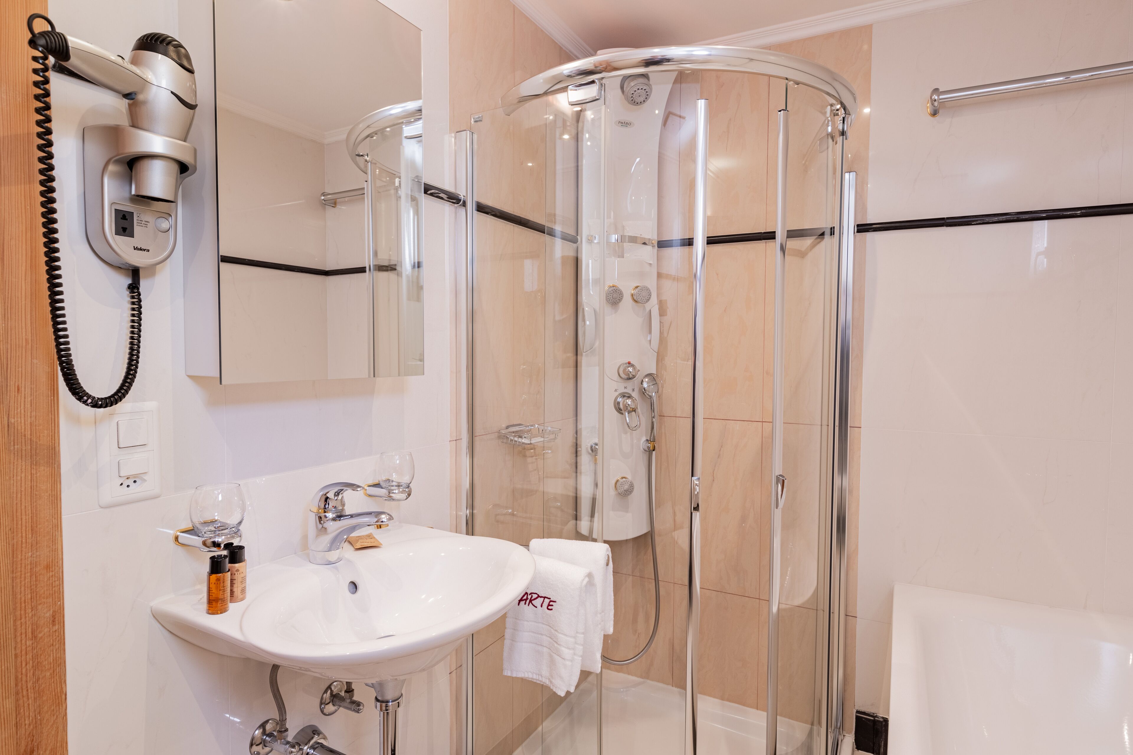 A modern bathroom with a glass-enclosed shower, a sink with a mirror, and a hairdryer mounted on the wall.
