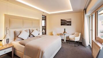 Ein modernes Hotelzimmer mit einem großen Bett, Nachttischen, einem kleinen runden Tisch, einem Sessel und einem Fenster mit Vorhängen.