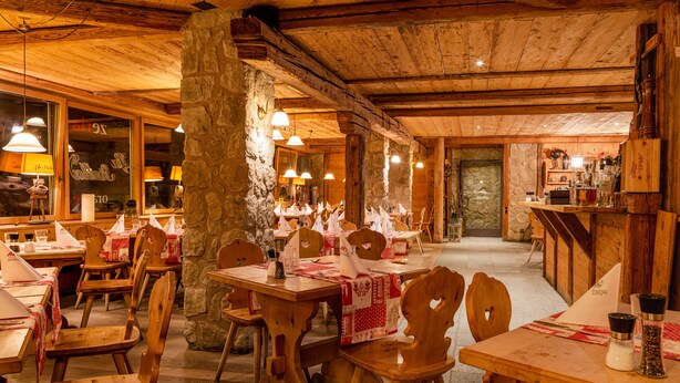 A rustic wooden interior with tables and chairs, stone pillars, and hanging lights. - Hotel Arte (St. Moritz)