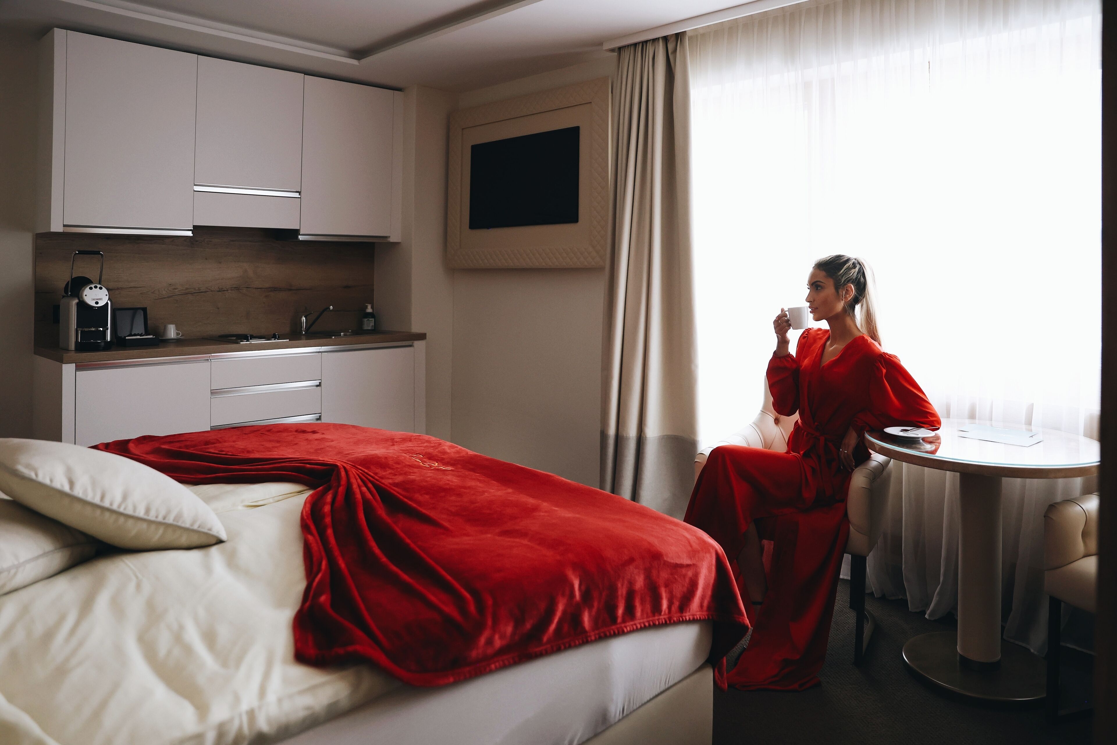 Una habitación de hotel con cama, escritorio, silla, televisión y ventana con cortinas.
